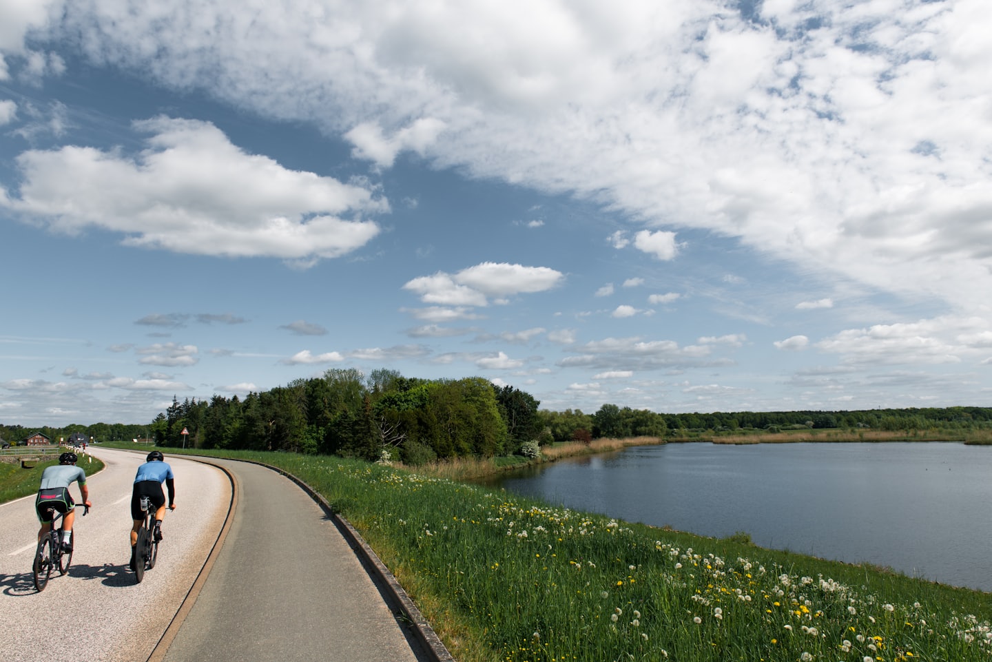 Dwóch rowerzystów jedzie malowniczą drogą wzdłuż wody.