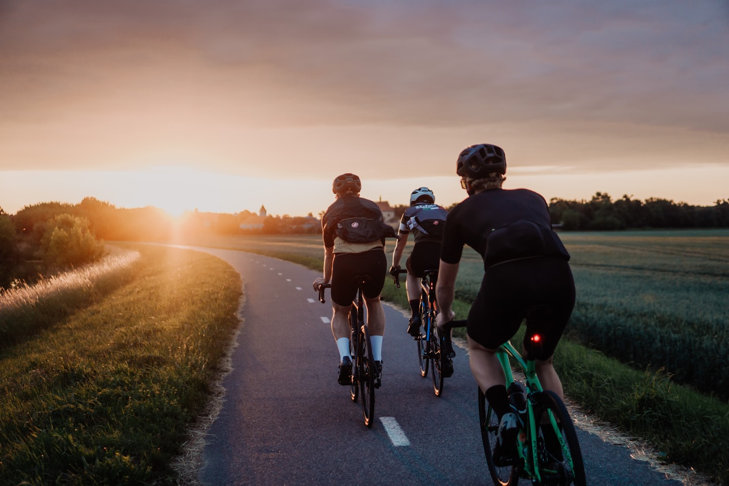 Rowerzyści jadą ścieżką przez pola o zachodzie słońca.